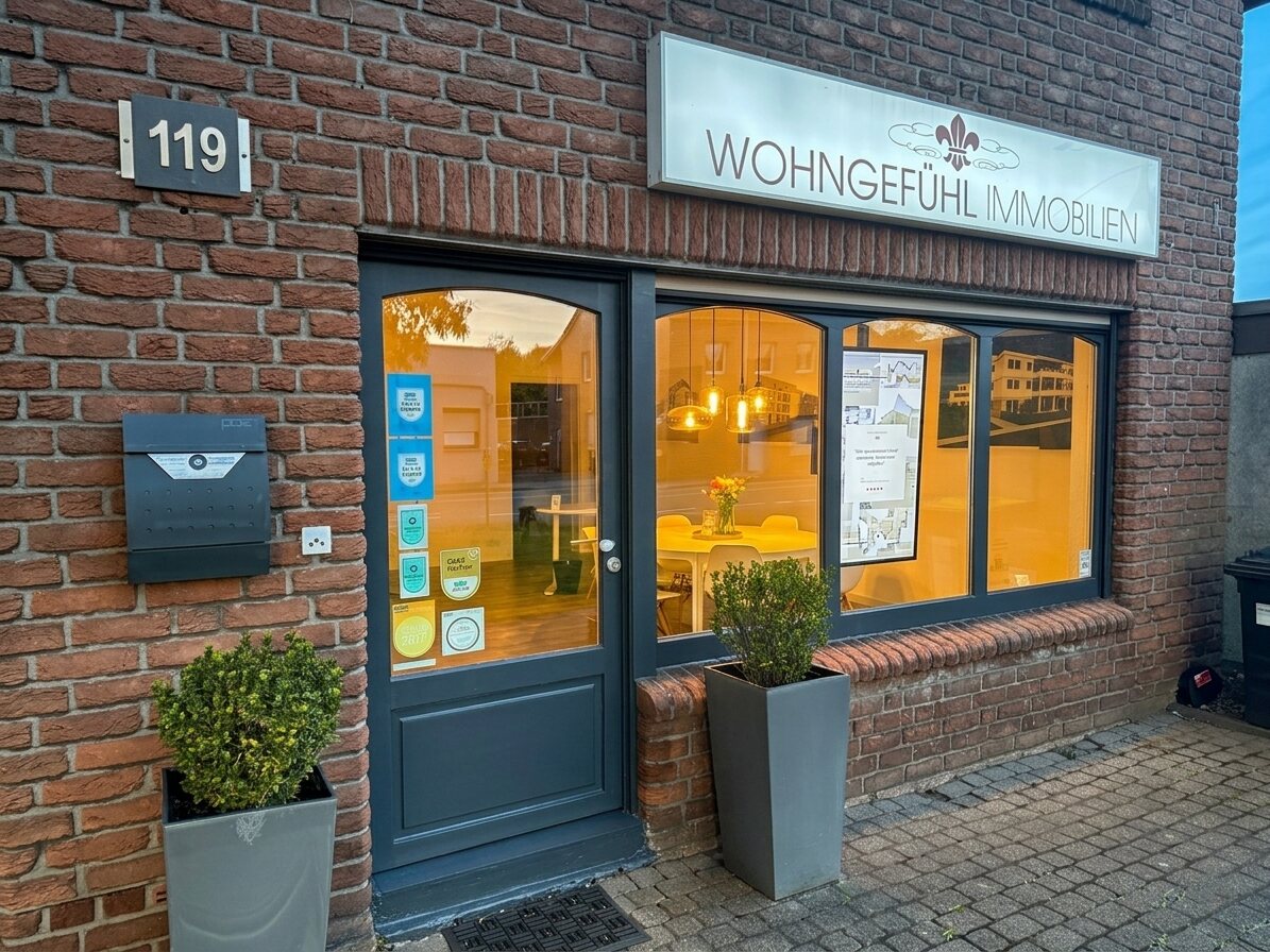 Die Maklerscreen-Box im echten Schaufenster von Wohngefühl Immobilien am Niederrhein: hochkant Display mit aktuellem Immobilien-Exposé und QR-Code unter dem beleuchteten Firmenschild.